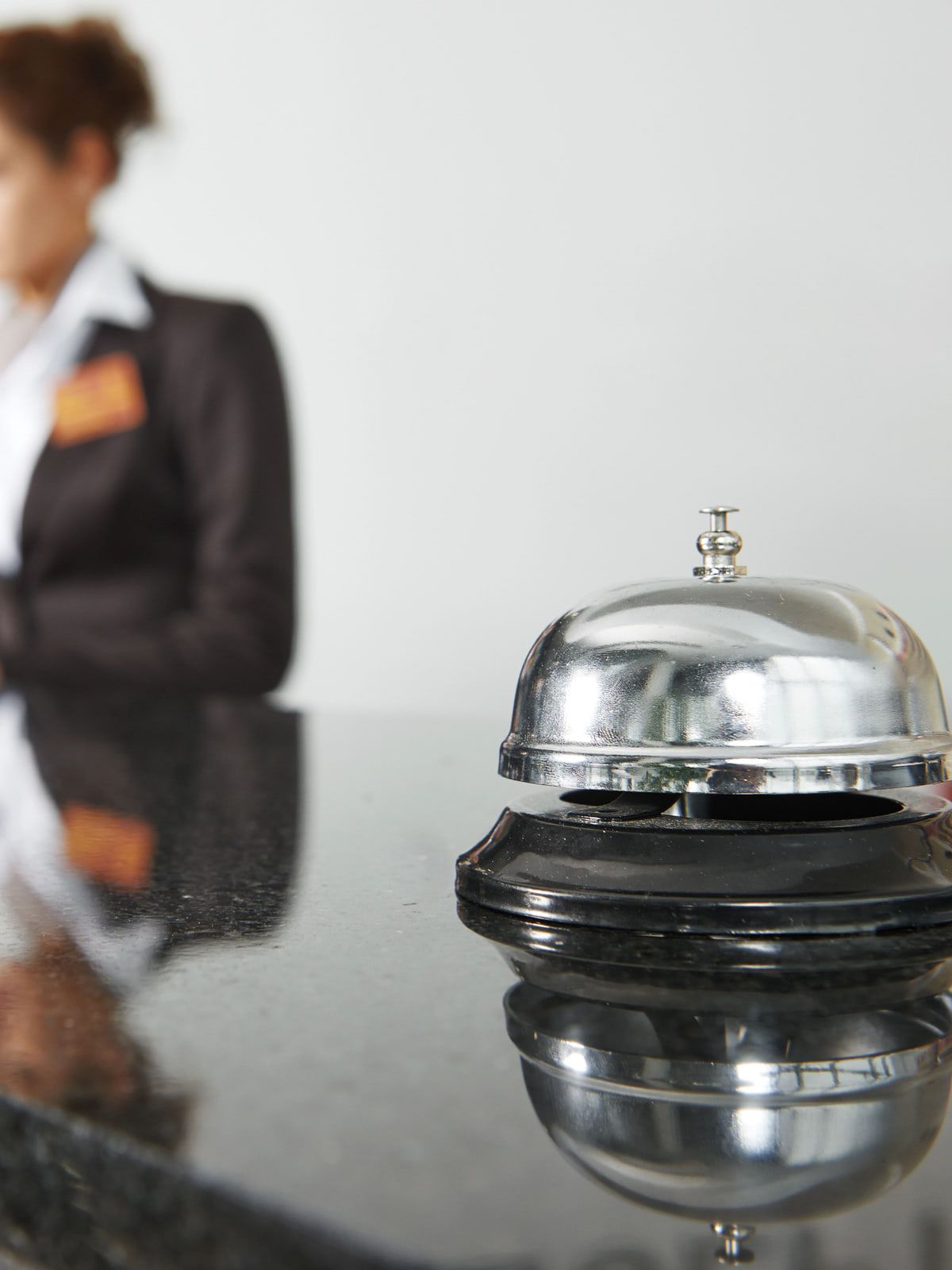 Recepcionistas de hotel uniformizadas atrás do balcão, com a sineta em primeiro plano