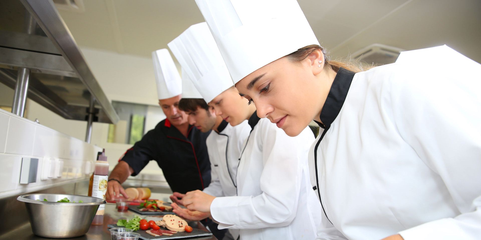 Cozinheiros de dólmã e toque blanche preparando pratos na cozinha profissional