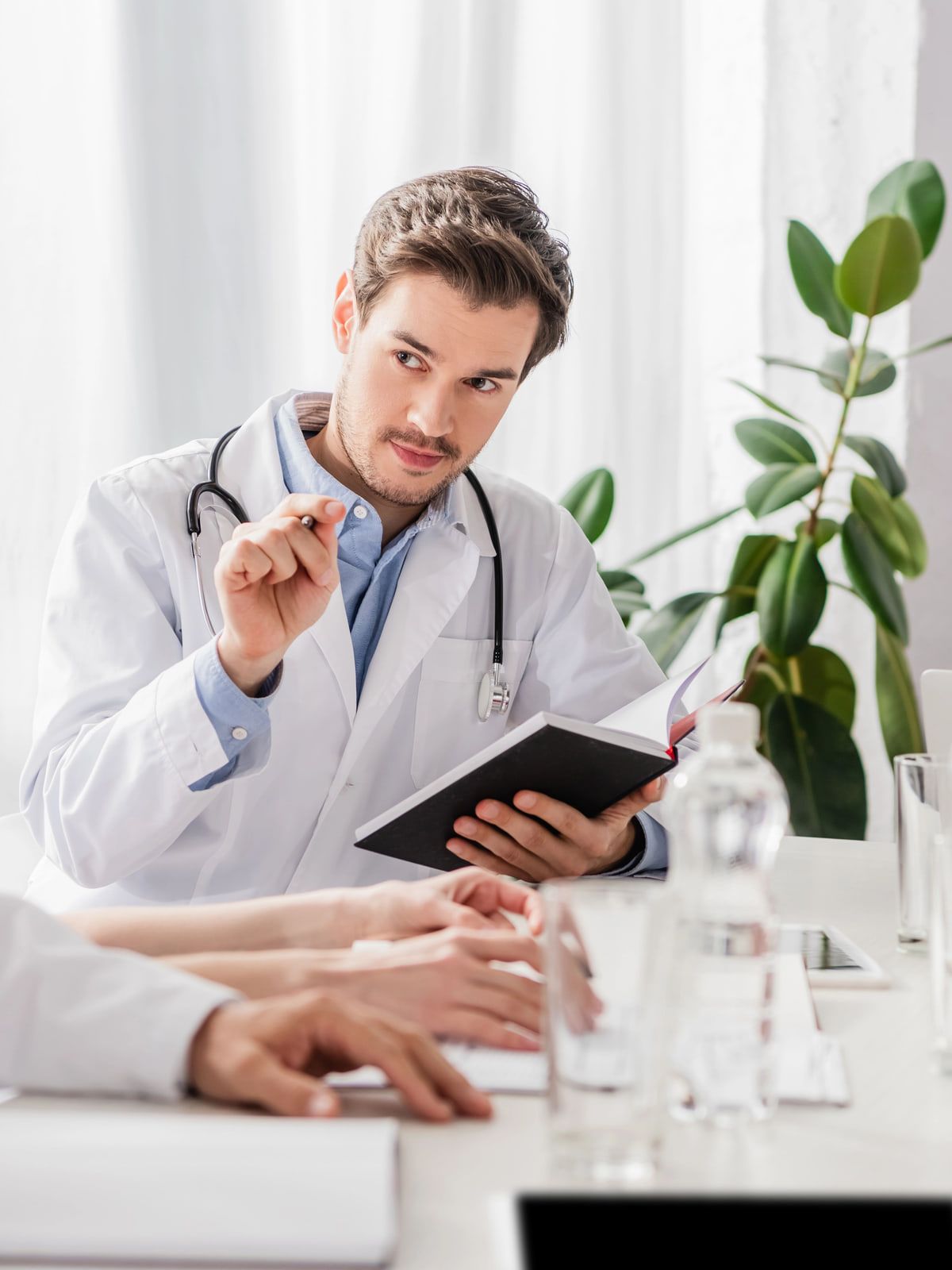 Médico de jaleco e enfermeira de scrub em reunião clínica