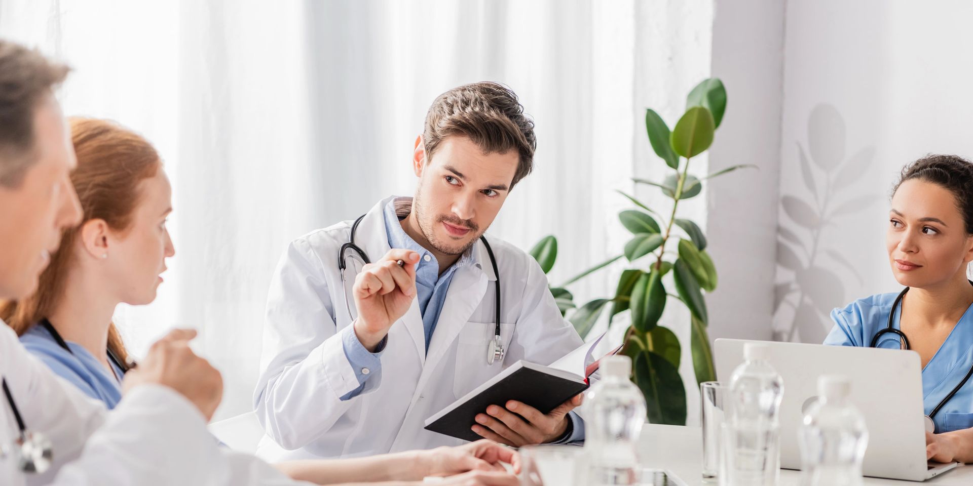 Médico de jaleco e enfermeira de scrub em reunião clínica